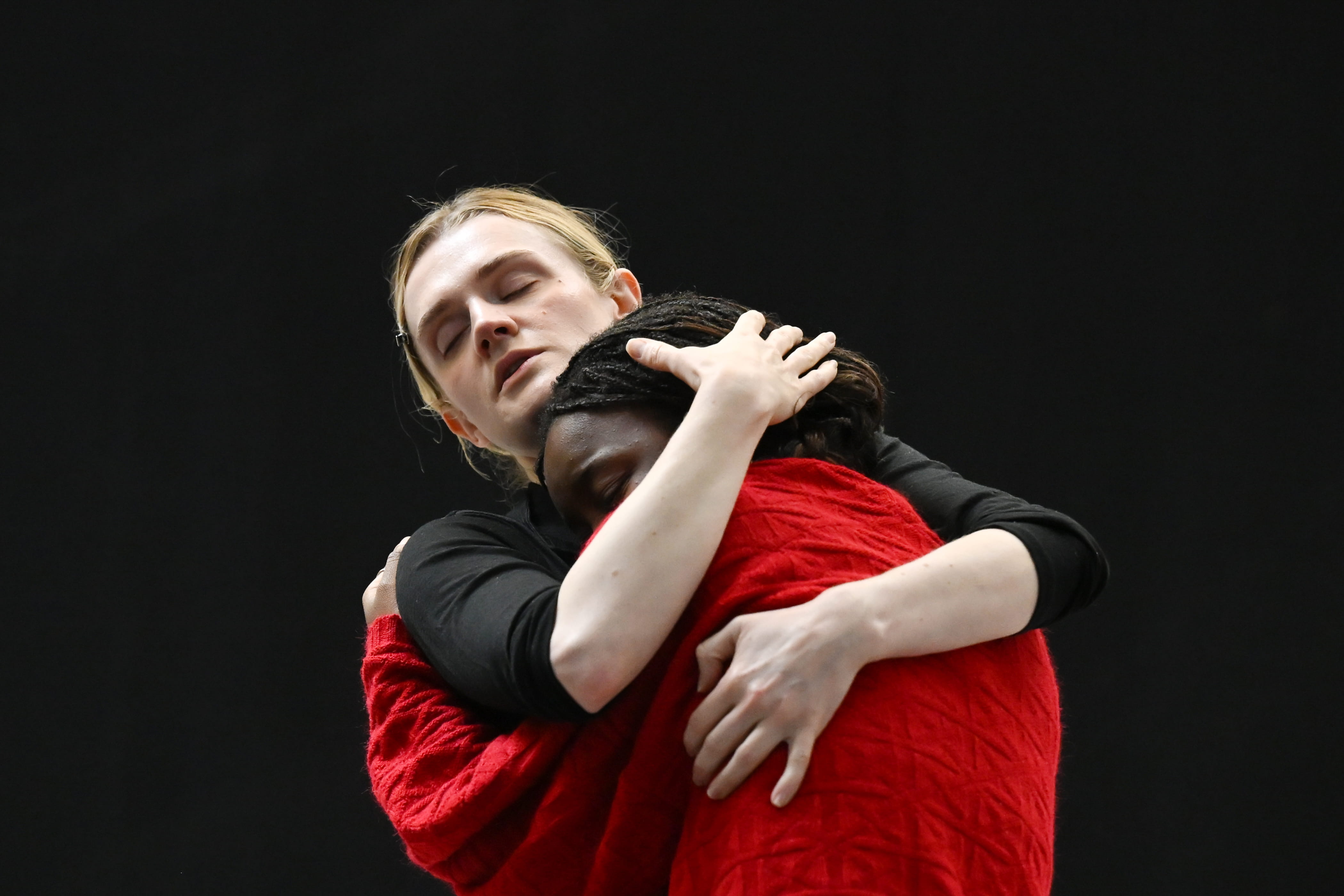 A woman is holding a girl in a close embrace. They are standing against a black backdrop.