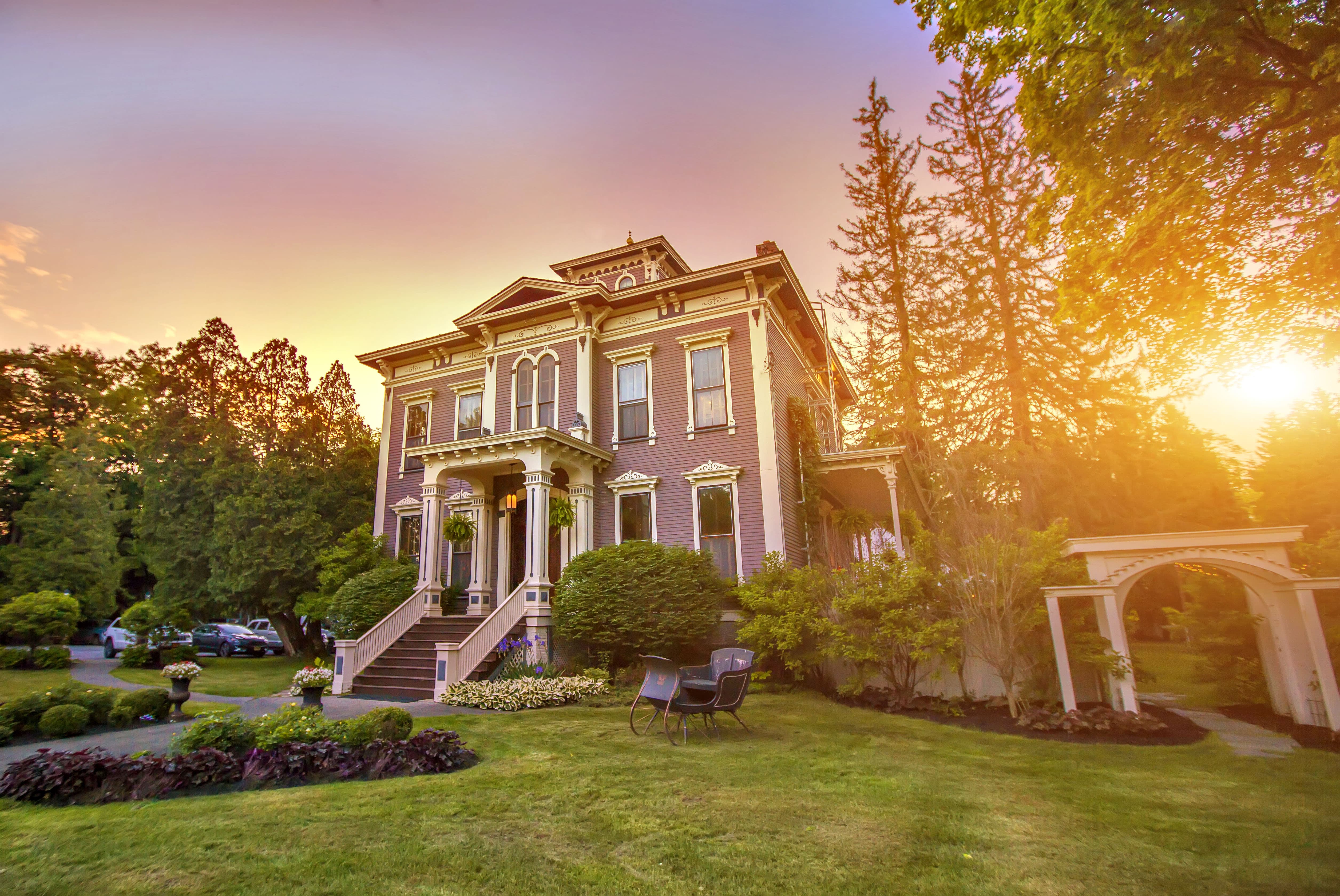 Sunset behind Victorian mansion with green lawn.