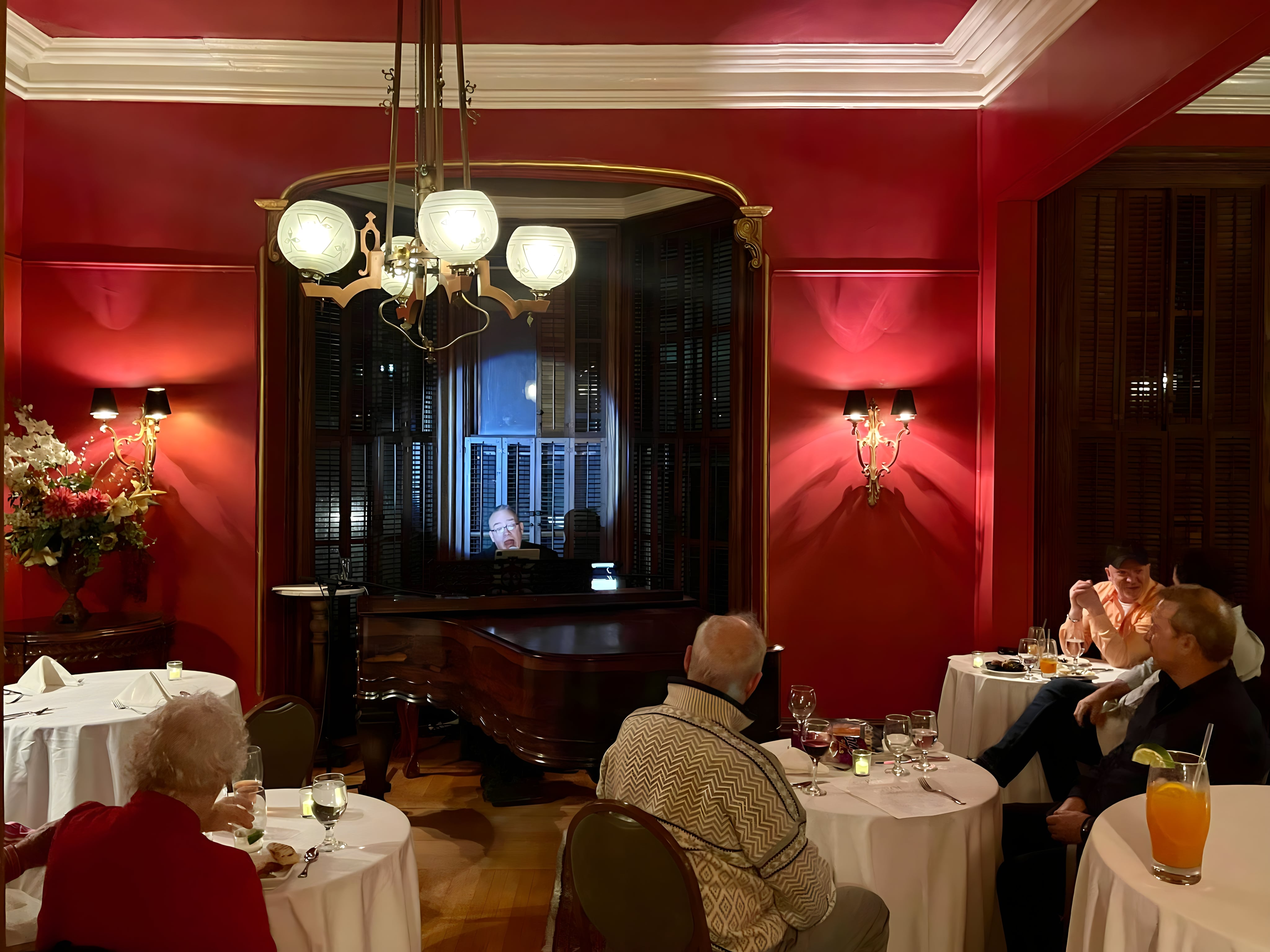 Man plays piano in spotlight as cabaret diners watch on