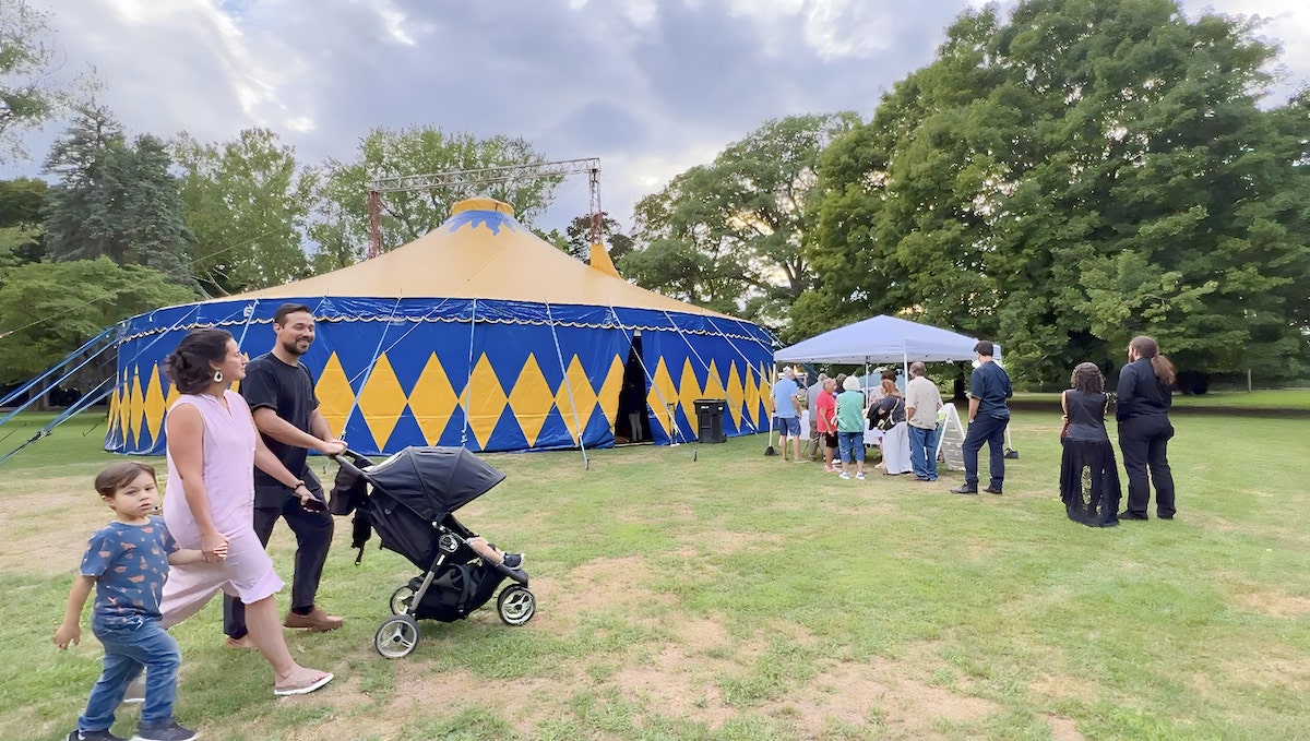 Family with small child and stroller approach line at big top circus tent. 